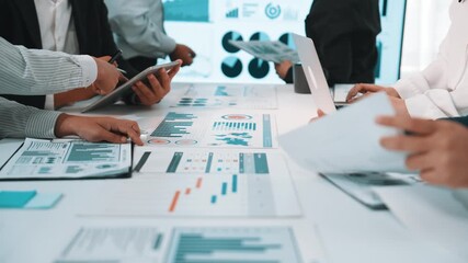 A diverse group of business professionals engages in a collaborative meeting, analyzing charts and data on devices in a modern office, emphasizing strategy and teamwork. SACTR - Powered by Adobe