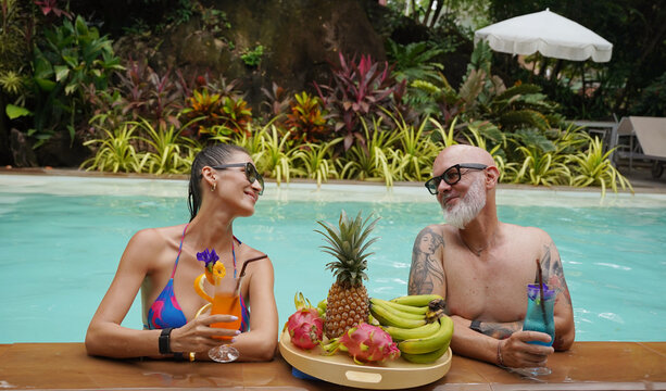 A man and a woman are having fun and drinking cocktails in the pool.