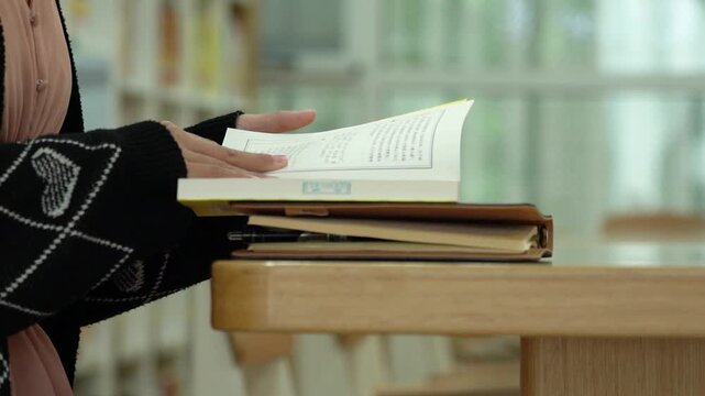 Student Flipping Pages in Library Book During Study Session