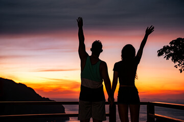 Fototapeta premium Happy young couple silhouette is standing with open arms against sunset sky and greeting sunset