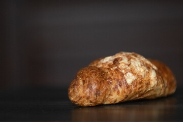 Freshly baked golden croissant resting on a dark wooden surface, showcasing flaky layers and a buttery texture, perfect for breakfast or pastry lovers