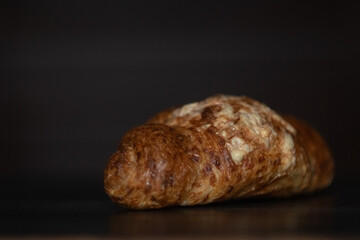 Freshly baked golden croissant resting on a dark wooden surface, showcasing flaky layers and a buttery texture, perfect for breakfast or pastry lovers