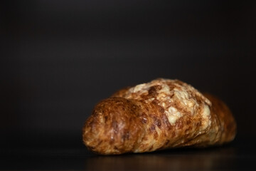 Freshly baked golden croissant resting on a dark wooden surface, showcasing flaky layers and a buttery texture, perfect for breakfast or pastry lovers