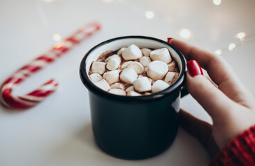 Woman's hands holding cup of Hot Chocolate with marshmallows at Christmas time.