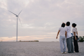 Fototapeta premium Three friends enjoying freedom and nature under a large wind turbine, celebrating together and embracing sustainable energy in an open landscape.