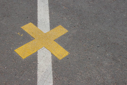 Yellow cross marking on asphalt surface, positioned between white lines, indicating a designated area for stopping or parking, enhancing urban street design and safety awareness - Powered by Adobe