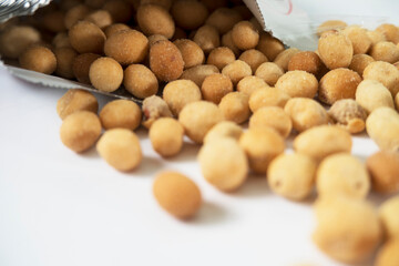 Crispy Coated Peanuts Spilling from Snack Package on White Background