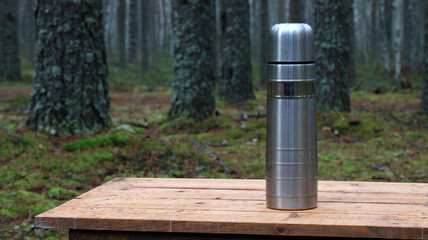 Naklejka premium Stainless steel thermos standing on wooden table in forest