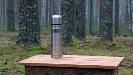Stainless steel thermos on wooden table in forest