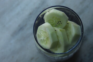 Healthy smoothie with cucumber pieces chopped into it. Health drink with green chopped fruit on a glass.