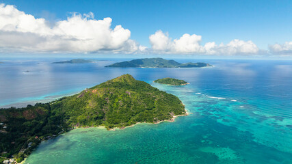 Fototapeta premium Aerial view of island with dense green vegetation sits amidst the turquoise waters. Praslin, Seychelles.