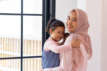 Happy Muslim mom with daughter and toy smiling at camera