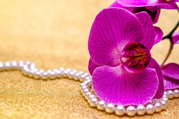 purple Orchid and pearl necklace on a shiny gold background
