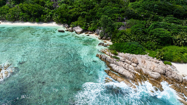 Granite formations meet clear turquoise waters along a white sandy beach surrounded by greenery. Seychelles, La Digue. - Powered by Adobe