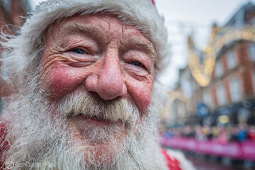 international Santa Dash participant close-up, red suit and fluffy white beard, sweaty but happy facial expression showing joy of the race, holiday street decorations blurred in the background