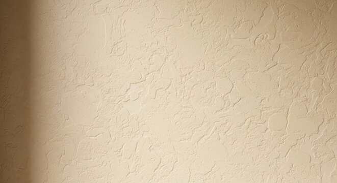 Close up of a beige textured wall surface with subtle shadow on left side