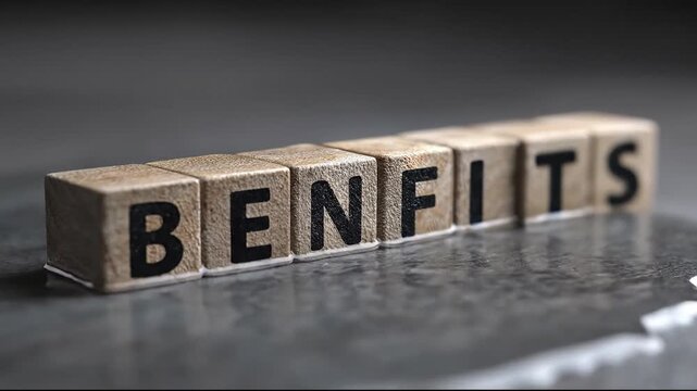 A close-up low-angle shot of wooden cubes with black letters spelling the word BENEFITS on a dark textured surface