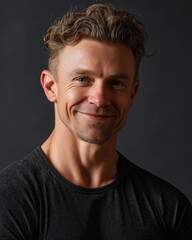 Fototapeta premium A smiling man with curly hair, wearing a dark shirt, poses confidently against a neutral background, showcasing a warm expression.