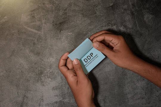 A close-up of a hand holding a blue note with the text &ldquo;DDP &ndash; Delivered Duty Paid,&rdquo; illustrating international trade terms, shipping responsibilities, and logistics concepts on a neutral textured back