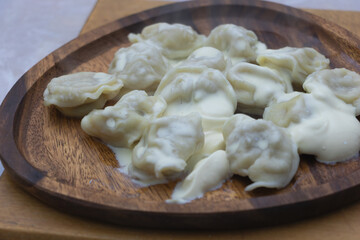 Dumplings with sour cream served on wooden plate