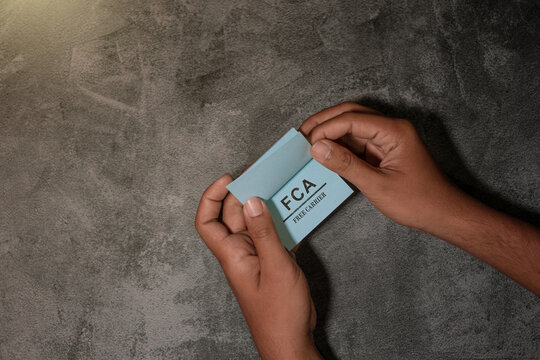 A hand holding a blue card displaying the term &ldquo;FCA &ndash; Free Carrier,&rdquo; representing international trade, shipping terms, logistics, and global commerce on a neutral background.
