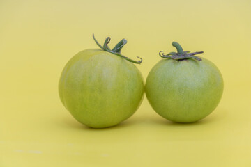 Green unripe tomatoes on yellow background