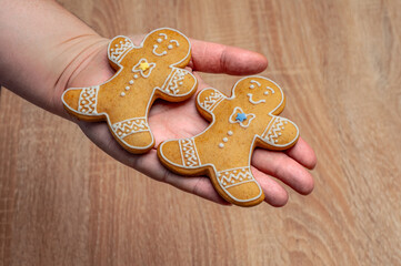 Two gingerbread men cookies held in a hand against a wooden background