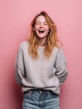 isolated shot of joyful blonde young cute woman laughs joyfully as hears funny anecdote from friend has long light hair poses against pink studio wall happiness and positive emotions concept no logos