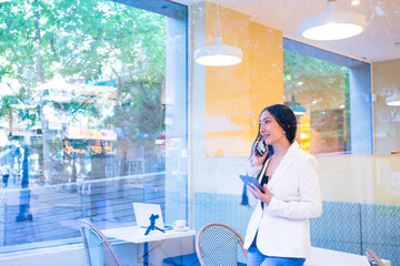 Businesswoman talking on phone working remotely in cafe