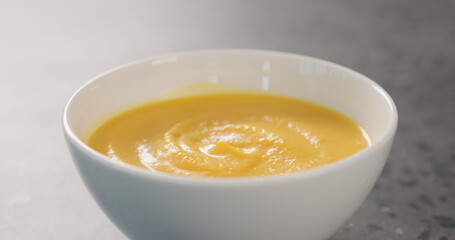 Pumpkin cream soup in white bowl on concrete background