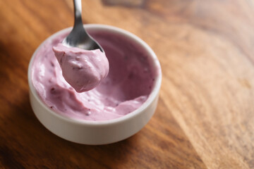 eating blueberry yogurt from white bowl on wood table