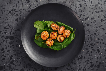 Seared scallops on pile of spinach on black plate top view