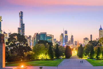 City skyline at dusk with lush green park and dramatic sunset sky