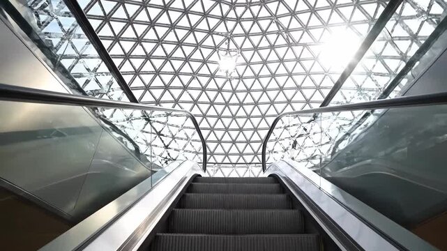 Empty escalators under a geodesic dome in a modern building with sunlight