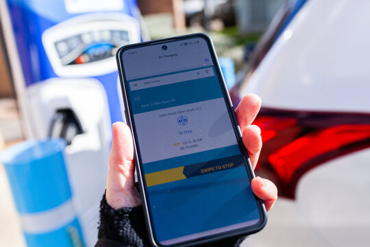 Person holding phone to use app for charging hybrid car at public charger
