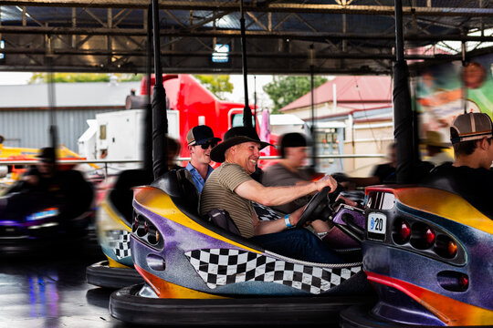 Middle aged man riding on dodgem cars show ride at event with teen son having fun together