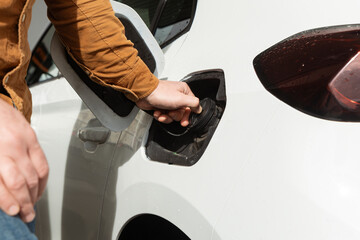 Person refueling a car at a gas station with fuel nozzle in hand and vehicle details visible