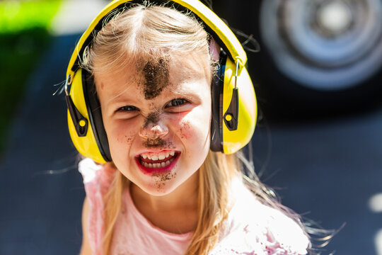 Child wearing earmuffs with face covered in dirt grinning outdoors