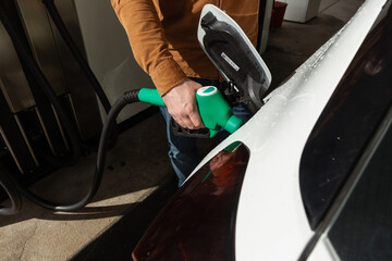 Person refueling a car at a gas station with green fuel nozzle in hand during daytime