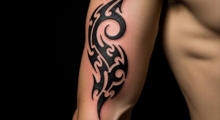 Close-up of a person's arm featuring a striking black tribal tattoo design against a dark background.