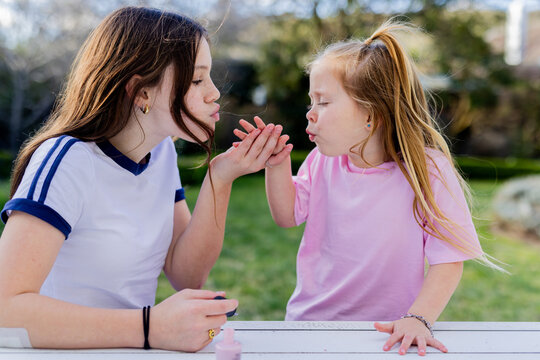 Preteen girl blowing young sisters fingers with nail polish to dry off