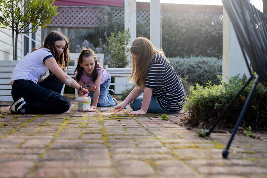 Young girls playing with colourful chalk on a brick floor of garden patio