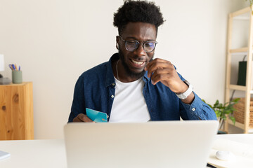 Happy African American man online shopping using laptop and credit card at home office.