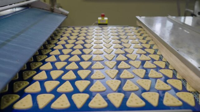 Triangle-shaped candies with holes resembling swiss cheese slices moving on an industrial conveyor belt, symbolizing food production