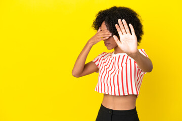 Young African American woman isolated on yellow background making stop gesture and covering face