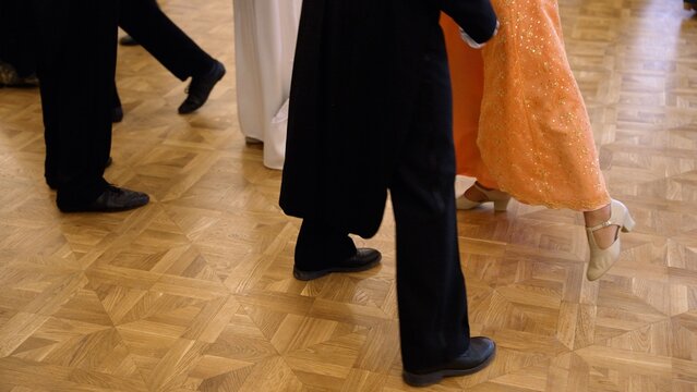 Elegant couples in 19th-century costumes dancing a lively polka on a wooden parquet floor during a historical reconstruction ball