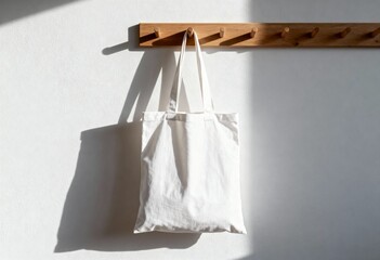 Mockup of white cotton tote bag hanging on wooden coat rack, sunny minimalist interior