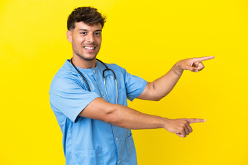 Young surgeon doctor man isolated on yellow background pointing finger to the side and presenting a...