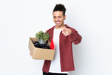 Caucasian man making a move while picking up a box full of things over isolated white background points finger at you with a confident expression