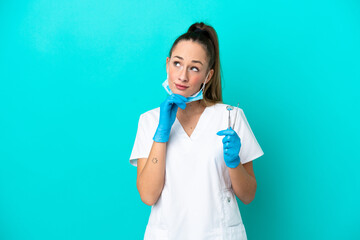 Dentist caucasian woman holding tools isolated on blue background and looking up